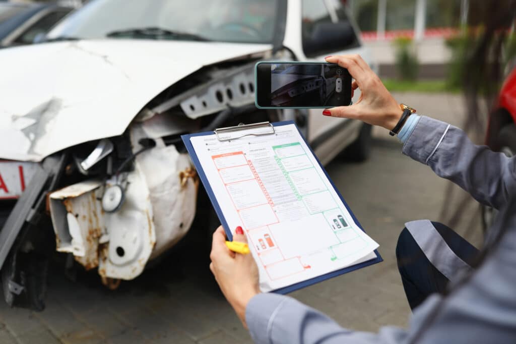Insurance agent takes pictures of crashed car on his smartphone and fills out the insurance